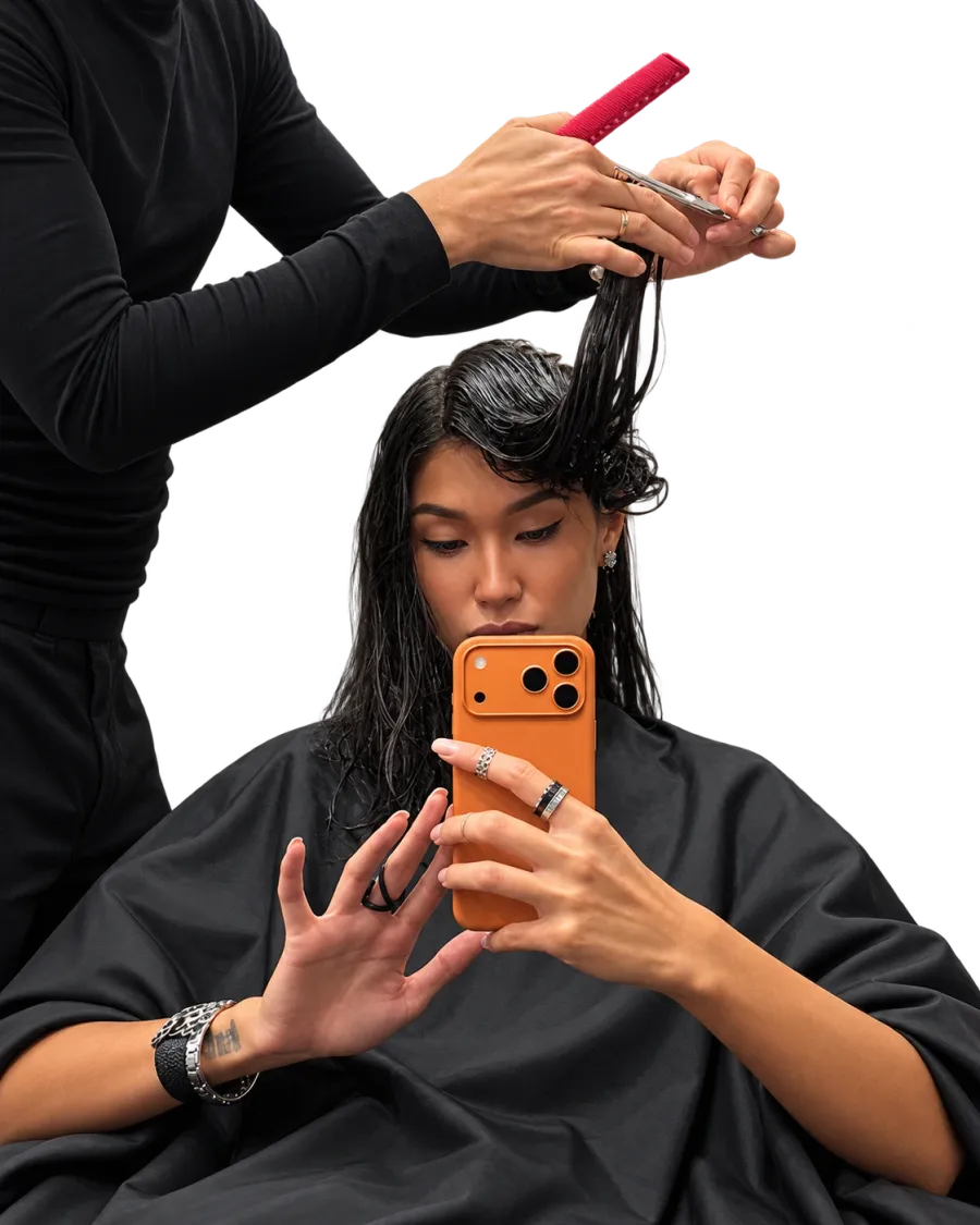 A client on her phone while her stylist cuts her hair.