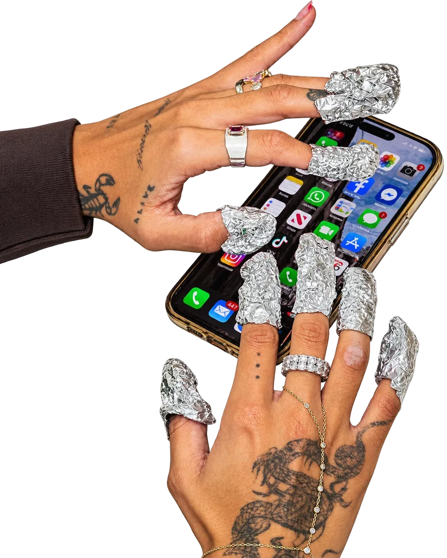 A client on her phone while her gel polish soaks off under foil.